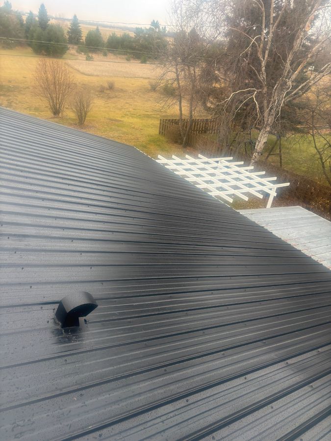 Completed metal roof with vent detail and prairie landscape